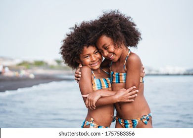 Black Sister Twins Having Fun On The Beach During Summertime - Little Female Kids Laughing And Hugging Each Others - Love And Family Union Concept - Main Focus On Right Chil Face