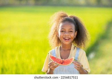 Black skinned cute little girl eating watermelon outdoors green rice field backdrop African child eating watermelon - Powered by Shutterstock