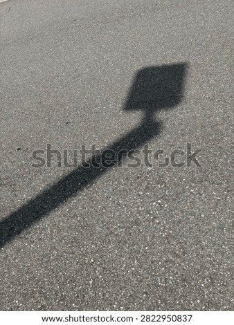 Black slanted lamp post light pole shadow on asphalt blacktop pavement 