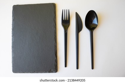 A Black Slate Plate With Eating Utensils. An Empty Sushi Plate On A White Table.