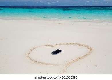 Black smartphone with empty screen display, Seashells and a sandy heart on the beach.
