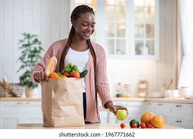 Black Smiling Lady Unpacking Paper Bag With Fresh Organic Vegetables And Fruits After Grocery Shopping, Happy African American Woman Standing In Cozy Kitchen Interior At Home, Copy Space - Powered by Shutterstock