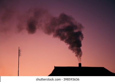 Black Smoke Comes Out Of A House's Chimney In Dusk.
