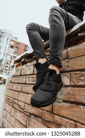 Black Sneakers Or Shoes And Grey Skinny Jeans On Men's Lags Close Up. Brick Wall Industrial Background