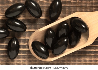 Black soft gel capsules in a spoon on wood background. Astaxanthin softgel pills. Natural red algae antioxidant. Vitamin E dietary supplement. Closeup, top view