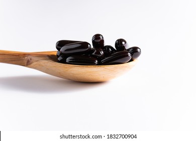 Black soft gel medical capsules in the wooden spoon on white background. Immunity support and health care concept.