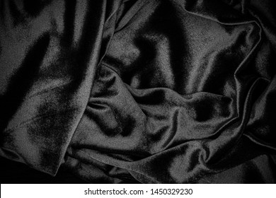 Black soft plush fabric with drapery. Dark velvet draped velour background.  Wrinkled cloth black fabric background.