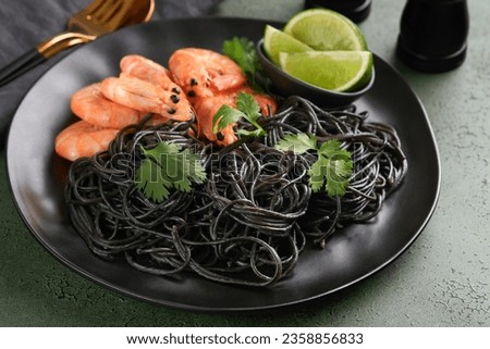 Black spaghetti pasta shrimp on black plate on dark concrete table background. Squid ink pasta with prawns. Pasta seafood. Top view on green stone table. Mediterranean traditional cuisine dish.