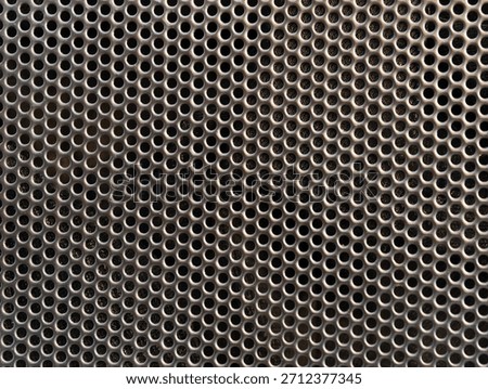 Black speaker grille background featuring small circular perforations arranged in a repeating pattern, creating a functional industrial surface with depth, texture, and modern audio equipment 