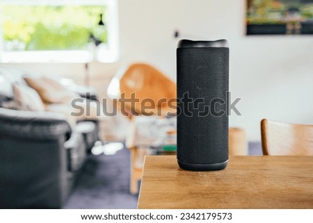 Black speaker on a wooden table. Couch, sofa, lamps on the background, cosy home
