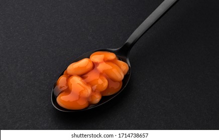 Black Spoon Of Baked Beans In Tomato Sauce Isolated On Black Background