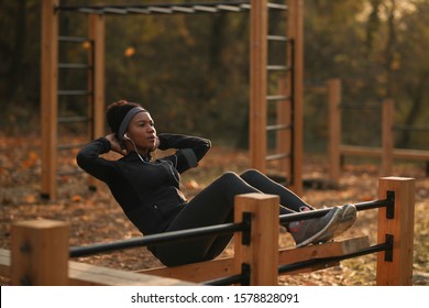 Black sportswoman exercising sit-ups while being at outdoor gym at the park.  - Powered by Shutterstock