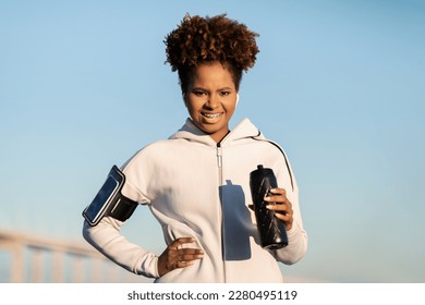 Black Sporty Female With Fitness Water Bottle In Hands Standing Outdoors, Happy African American Woman In Activewear Ready For Fitness Workout Or Jogging Outside, Enjoying Healthy Lifestyle - Powered by Shutterstock