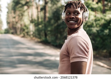 Black sporty man, dressed in sportswear listening to music on headphones during morning workout, African American man exercising in tropical park enjoying music - Powered by Shutterstock