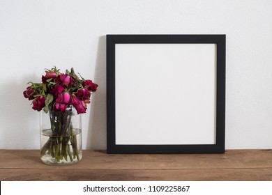 Black Square Frame With Withered Rose Flowers In Vase On Table