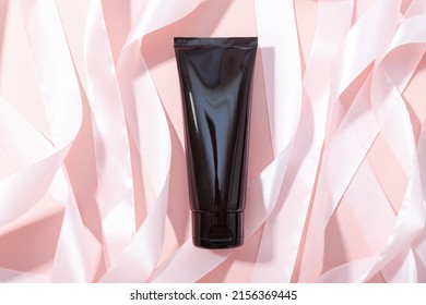 Black Squeeze Bottle Cosmetic Tube And Pink Ribbons On Pink Background, Mockup. Daily Cream, Gel, Skin Care, Sunscreen, Moisturizer. Front View, Blank Bottle.