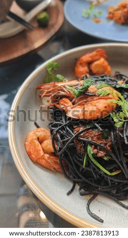 Black squid ink spaghetti entwines with plump prawns, creating a visually striking dish with briny richness and delicate oceanic flavors. 