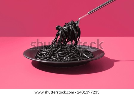 Black squid ink spaghetti on a plate with fork on pink background