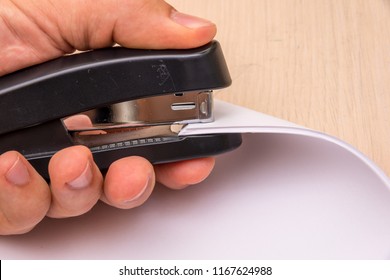 A black stapler in his hand pierces many sheets of paper