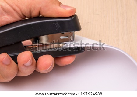 A black stapler in his hand pierces many sheets of paper