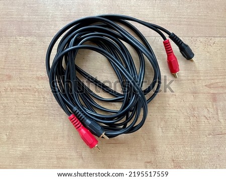 Black, stereo audio cable with red and black plastic covers over gold-plated phono connectors on both ends, on smooth wooden surface