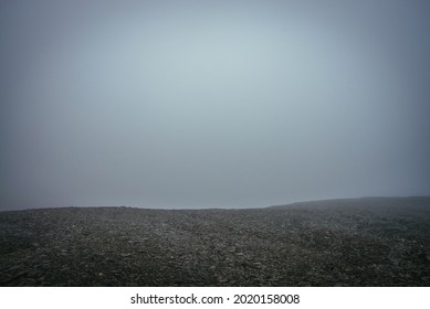 Black stone field in dense fog in highlands. Empty stone desert in thick fog. Zero visibility in mountains. Minimalist nature background. Dark atmospheric foggy mountain landscape. Foggy minimalism.