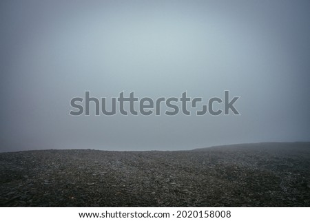 Black stone field in dense fog in highlands. Empty stone desert in thick fog. Zero visibility in mountains. Minimalist nature background. Dark atmospheric foggy mountain landscape. Foggy minimalism.
