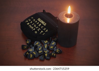 Black stone runes with black candle on wooden background. - Shutterstock ID 2364715259