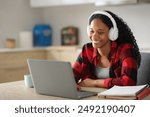 Black student e-learning with laptop and headphone in the kitchen at home