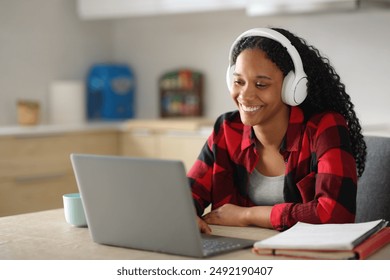 Black student e-learning with laptop and headphone in the kitchen at home - Powered by Shutterstock