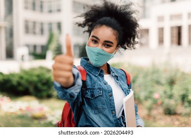 Black Student Girl Wearing Face Mask Gesturing Thumbs Up Approving College Standing Outdoors Near University Building. I Like Studentship And Education During Covid-19 Epidemic. Selective Focus