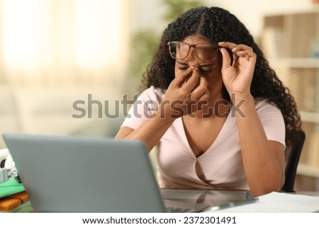 Black student suffering eyestrain studying with a laptop at home