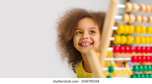 A Black student in a yellow dress laughs brightly behind a colored abacus in an elementary school classroom - Powered by Shutterstock