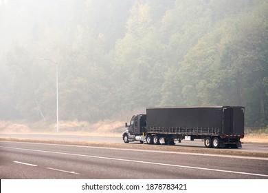Black Stylish Industrial Grade Big Rig Semi Truck With Covered Dry Van Semi Trailer Transporting Commercial Cargo Driving On The Unhealthy Road In The Thick Smog From A Disaster Extensive Forest Fire