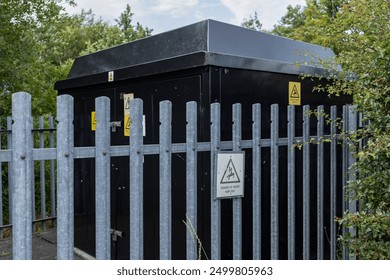 Black suburban electricity substation with galvanized metal fence, hedge, and danger keep out signs - Powered by Shutterstock