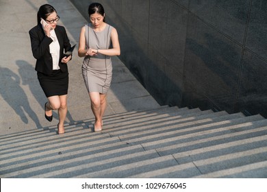 black suit office lady talking cellphone and the grey dress businesswoman looking at her watch. These two busy successful Asian are going to train station and now waiting for someone. - Shutterstock ID 1029676045