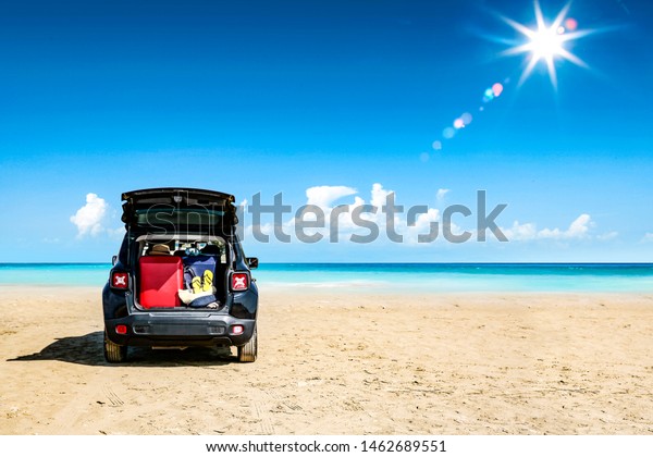 Black summer car on beach with suitcase and ocean\
landscape. Blue sky and sun\
