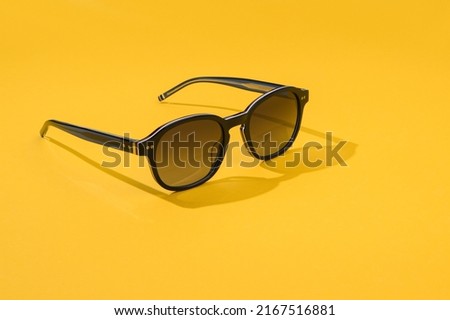 Black sunglass with oval frame, polarizing lenses. Sunglasses in beautiful fashion concept summer beach accessories. Sunglasses in sunlight on pastel blue color background. Front view