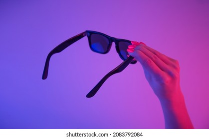 Black sunglasses in female hand and bright orange manicure in trendy neon light 