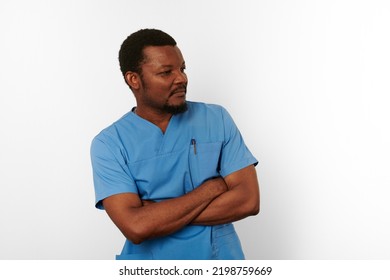 Black Surgeon Doctor Bearded Man In Blue Coat With Crossed Arms Isolated On White Background Copy Space. Serious Adult Black African American Practicing Surgeon Portrait, Confident Look To Right