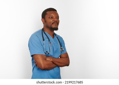 Black Surgeon Doctor Bearded Man In Blue Coat With Crossed Arms Isolated On White Background Copy Space. Serious Adult Black African American Practicing Surgeon Portrait, Confident Look To Right