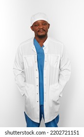 Black Surgeon Doctor Bearded Man In White Coat And White Cap With Hands In Pockets Isolated On White Background. Serious Adult Black African American Practicing Surgeon Portrait, Confident Look