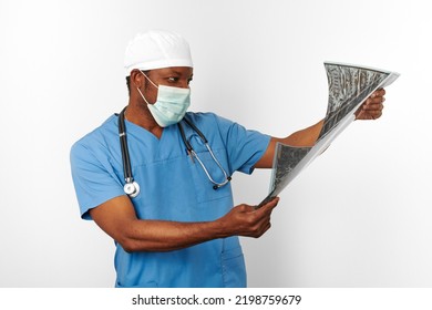 Black Surgeon Doctor Man In Blue Coat White Cap And Surgeon Mask Holds X Ray Image Isolated On White Background. Pensive Adult Black African American Practicing Surgeon Portrait, Thoughtful Look