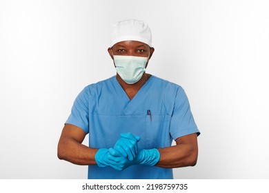 Black Surgeon Doctor Man In Blue Coat White Cap Surgeon Mask Sterilizes Blue Gloves With Aseptic Technique, Isolated On White Background. Adult Black African American Practicing Surgeon Portrait