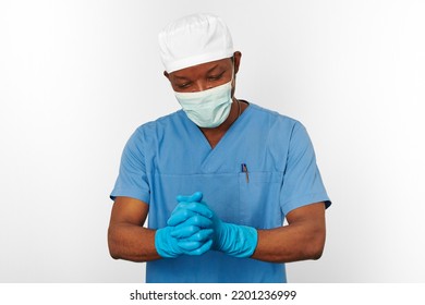 Black Surgeon Doctor Man In Blue Coat White Cap Surgeon Mask Sterilizes Blue Gloves With Aseptic Technique, Isolated On White Background. Adult Black African American Practicing Surgeon Portrait