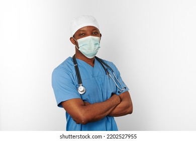 Black Surgeon Doctor Man In Blue Coat White Cap And Surgeon Mask With Crossed Arms Isolated On White Background. Focused Adult Black African American Practicing Surgeon Portrait, Confident Look