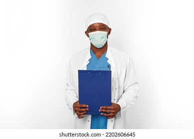 Black Surgeon Doctor Man In White Coat Cap And Surgeon Mask Holds Medical Records With Diagnosis On Clipboard, Isolated On White Background. Adult Black African American Practicing Surgeon Portrait