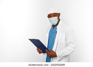 Black Surgeon Doctor Man In White Coat Cap And Surgeon Mask Holds Medical Records With Diagnosis On Clipboard, Isolated On White Background. Adult Black African American Practicing Surgeon Portrait