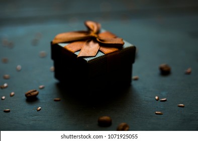 Black Surprise Box. Brown Bow. Surprice For Darlin Love. Blur Dark Studio Background Of Black Table. Professional Photo Session. Professional Photo Studio. Some Coffee Beans On Black Table