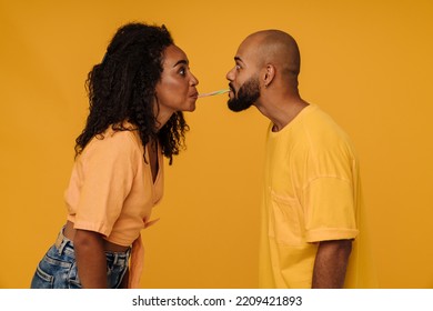 Black Surprised Man And Woman Eating Candy Together Isolated Over Yellow Background